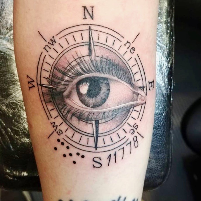 Image: Picture of Alison's tattoo. It is an Intricate black illustration of a compass. In the middle Of the compass is an eye with long lashes. The compass is marked with letters representing North, south, east, and west.